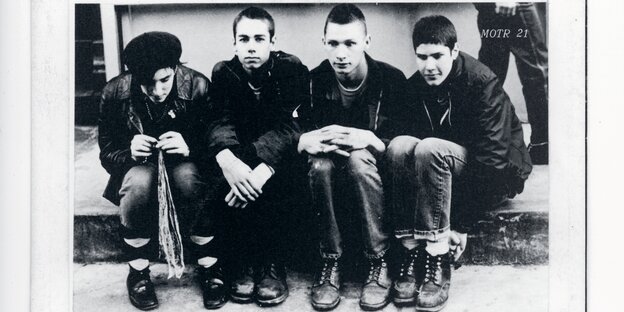 Ein schwarz-weiß Foto, auf dem vier junge Männer, die Band "Beastie Boys" nebeneinander sitzen Ein schwarz-weiß Foto, auf dem vier junge Männer, die Band "Beastie Boys" nebeneinander sitzen