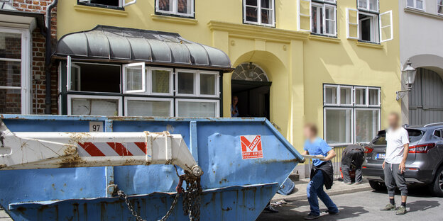 Vor einem Altbau füllen zwei Männer einen Bauschuttcontainer. Vor einem Altbau füllen zwei Männer einen Bauschuttcontainer.