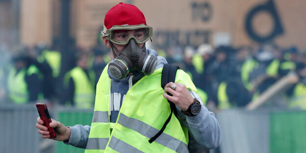 Ein Gelbwesten-Protestler mit Gasmaske und einem Smartphone in der Hand Ein Gelbwesten-Protestler mit Gasmaske und einem Smartphone in der Hand