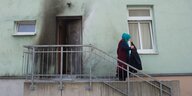 Eine Frau mit Kopftuch geht eine Treppe hinunter, an dem Gebäude sind Spuren eines Brandanschlags zu sehen