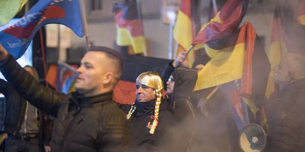 Menschen schwenken Deutschland- und AfD-Fahnen. Ein Mann trägt eine Perücke mit blonden Zöpfen Menschen schwenken Deutschland- und AfD-Fahnen. Ein Mann trägt eine Perücke mit blonden Zöpfen