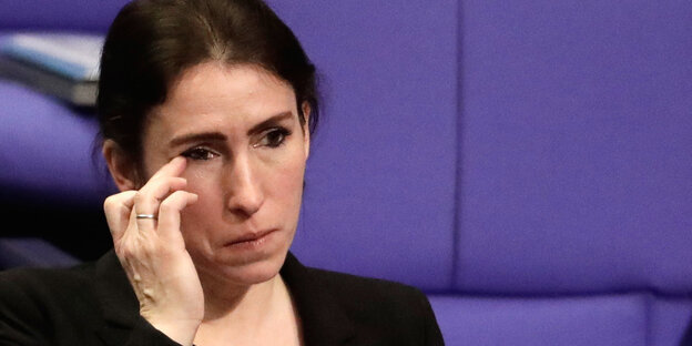 Eine brunette Frau im schwarzen Blazer sitzt im Parlament und hat einen Finger am Auge Eine brunette Frau im schwarzen Blazer sitzt im Parlament und hat einen Finger am Auge