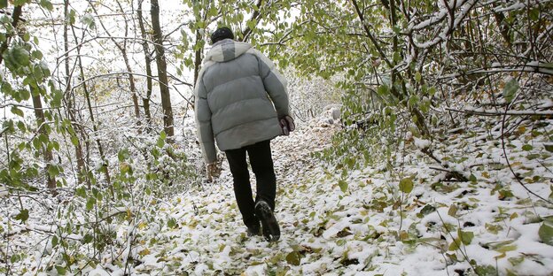 Ein Mann in Winterjacke geht über schneebedeckten Boden zu einem Zelt