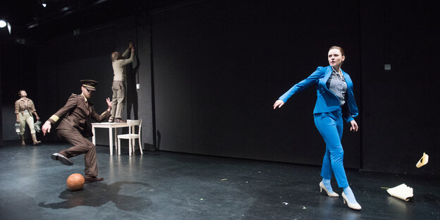 Auf der Bühne des Osnabrücker emma-Theaters spielt ein Soldat Fußball und eine Frau in blauem Trainingsazug marschiert von links nach rechts. Auf der Bühne des Osnabrücker emma-Theaters spielt ein Soldat Fußball und eine Frau in blauem Trainingsazug marschiert von links nach rechts.