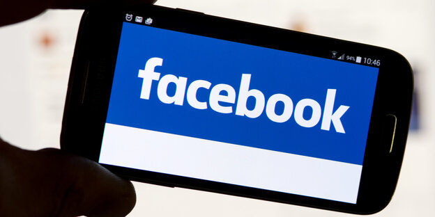 Facebook-Logo auf einem Smartphone, das von zwei Fingern gehalten wird Facebook-Logo auf einem Smartphone, das von zwei Fingern gehalten wird
