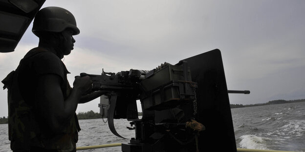 Ein nigerianischer Soldat mit Geschütz auf einem Boot Ein nigerianischer Soldat mit Geschütz auf einem Boot