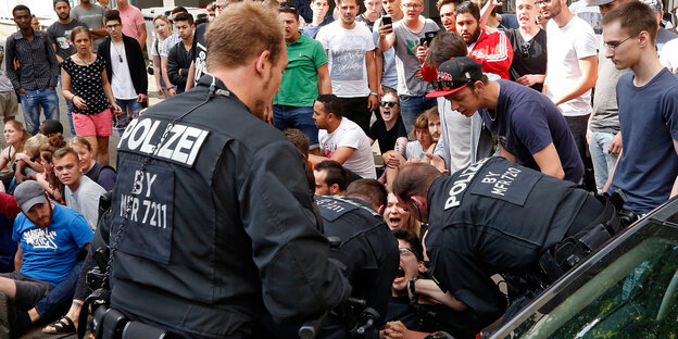 Polizisten beugen sich über auf dem Schulhof sitzende, schreiende Schüler