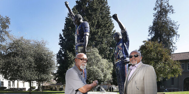 Tommie Smith und John Carlos stehen vor dem Denkmal, der sie in ihrer Pose mit ausgestreckter Faust bei der Siegerehrung zeigt Tommie Smith und John Carlos stehen vor dem Denkmal, der sie in ihrer Pose mit ausgestreckter Faust bei der Siegerehrung zeigt