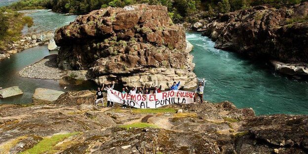 Eine Protestgruppe steht vor einem Fluß und hält ein Banner hoch Eine Protestgruppe steht vor einem Fluß und hält ein Banner hoch
