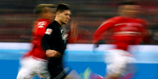 Ein Fußballer läuft nach rechts, gefolgt von zwei Gegenspielern Ein Fußballer läuft nach rechts, gefolgt von zwei Gegenspielern