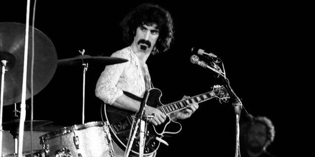 Frank Zappa steht vor einem Mikrofon und hat eine Gitarre in der Hand Frank Zappa steht vor einem Mikrofon und hat eine Gitarre in der Hand