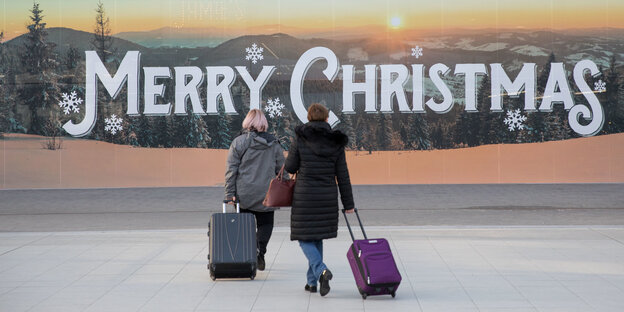 Reisende vor einem "Merry Christmas"-Schriftzug Reisende vor einem "Merry Christmas"-Schriftzug