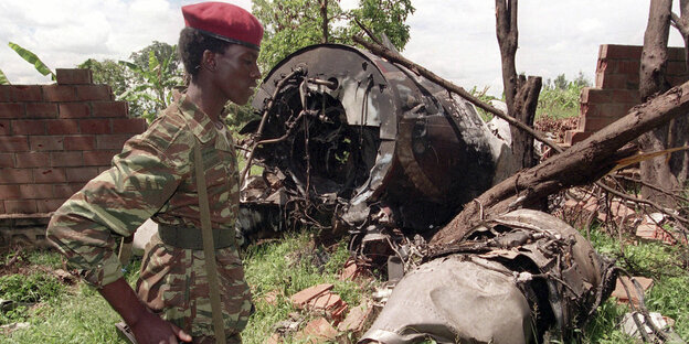 Mann in Tarnuniform und mit rotem Barrett vor einem Flugzeugwrack Mann in Tarnuniform und mit rotem Barrett vor einem Flugzeugwrack