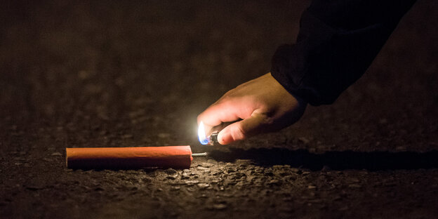 Eine Hand mit brennendem Feuerzeug nähert sich einem Böller