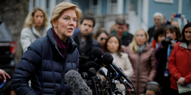 Elizabeth Warren spricht in mehrere Mikrofone, hinter ihr stehen viele Menschen Elizabeth Warren spricht in mehrere Mikrofone, hinter ihr stehen viele Menschen