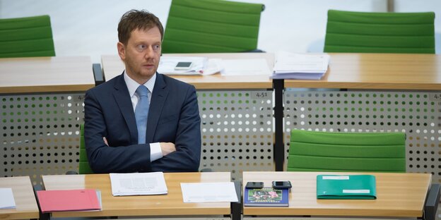 Ein Mann in Anzug und Krawatte sitzt mit verschränkten Armen hinter einem Konfernztisch Ein Mann in Anzug und Krawatte sitzt mit verschränkten Armen hinter einem Konfernztisch