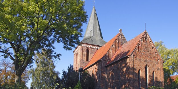 Eine Kirche aus roten Backsteinen, im Vordergrund steht ein Baum