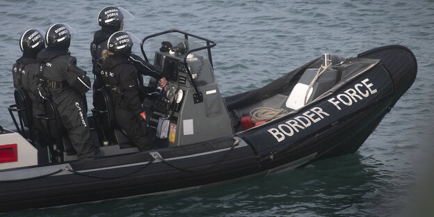 Vier Menschen in schwarzen Anzügen und Helmen auf einem schwarzen Schlauchboot auf offenem Meer Vier Menschen in schwarzen Anzügen und Helmen auf einem schwarzen Schlauchboot auf offenem Meer