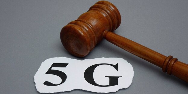 ein Auktionshammer liegt auf einer grauen Fläche, daneben ein Stück Papier, mit „5g“ beschriftet