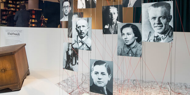 Historische Portraitfotos hängen von der Decke und sind mit Fäden mit einem Stadtplan verbunden. Historische Portraitfotos hängen von der Decke und sind mit Fäden mit einem Stadtplan verbunden.