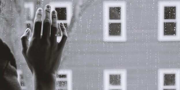 Eine Schwazweißbild zeigt eine Frauenhand, die an einer Fensterscheibe mit Regentropfen lehnt Eine Schwazweißbild zeigt eine Frauenhand, die an einer Fensterscheibe mit Regentropfen lehnt