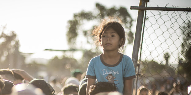 Migranten an der US-Grenze. Ein kleines Mädchen sitzt auf den Schultern eines Erwachsenen Migranten an der US-Grenze. Ein kleines Mädchen sitzt auf den Schultern eines Erwachsenen