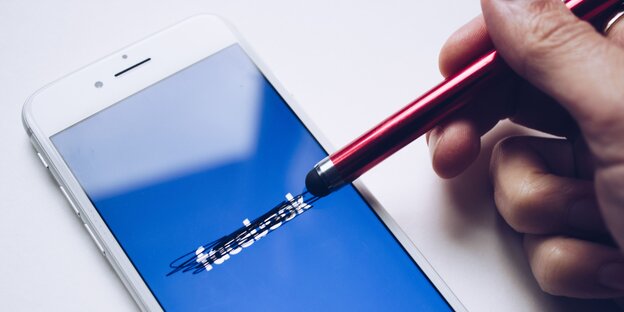 Ein weißes Smartphone, auf dem Bildschirm ist der Schriftzug Facebook zu lesen, der von einem Stift durchgestrichen wird. Ein weißes Smartphone, auf dem Bildschirm ist der Schriftzug Facebook zu lesen, der von einem Stift durchgestrichen wird.