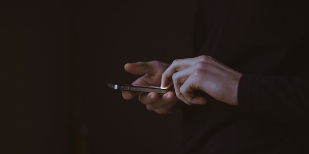 Hände berühren ein Iphone vor schwarzem Hintergrund Hände berühren ein Iphone vor schwarzem Hintergrund