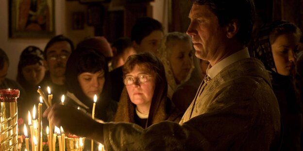 Brennende Kerzen und ein Preister und Gläubige auf einer Weihnachtsfeier in der russisch-orthodoxen Kirche der Heiligen Konstantin und Helena in Berlin-Tegel