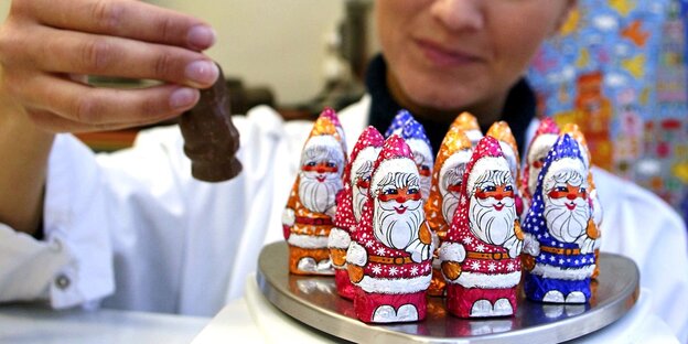 Eine Frau nimmt einen von mehreren Weihnachtsmännern aus Schokolade in die Hand. Eine Frau nimmt einen von mehreren Weihnachtsmännern aus Schokolade in die Hand.