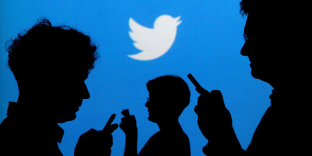Menschen halten Smartphones in der Hand, im Hintergrund ist der Twitter-Vogel zu sehen Menschen halten Smartphones in der Hand, im Hintergrund ist der Twitter-Vogel zu sehen