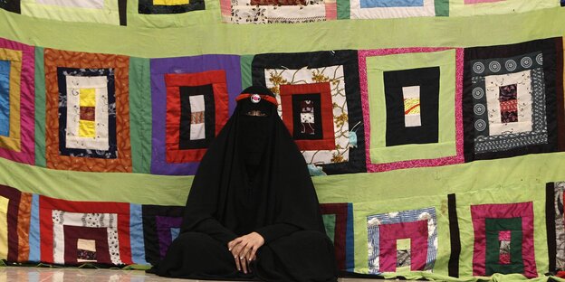 Eine vollverschleierte Frau sitzt vor einem Wandschmuck Eine vollverschleierte Frau sitzt vor einem Wandschmuck
