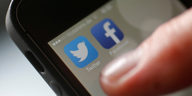 Ein Finger auf einem Smartphone, dessen Bildschirm die Apps von Twitter und Facebook zeigt Ein Finger auf einem Smartphone, dessen Bildschirm die Apps von Twitter und Facebook zeigt