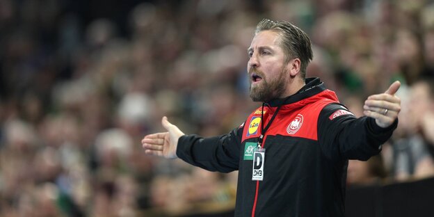Ein Mann steht am Spielfeldrand und breitet die Arme aus, hinter ihm Tribünen Ein Mann steht am Spielfeldrand und breitet die Arme aus, hinter ihm Tribünen