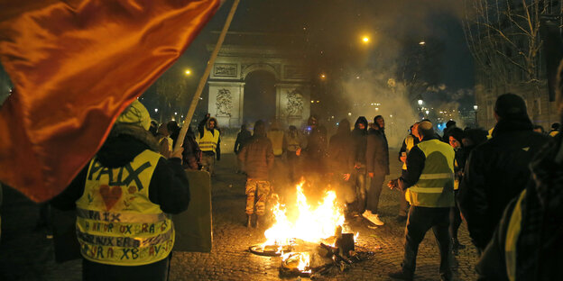 DemonstrantInnen mit gelben Westen stehen neben einem brennenden Fahrrad auf der Avenue des Champs-Elysée DemonstrantInnen mit gelben Westen stehen neben einem brennenden Fahrrad auf der Avenue des Champs-Elysée
