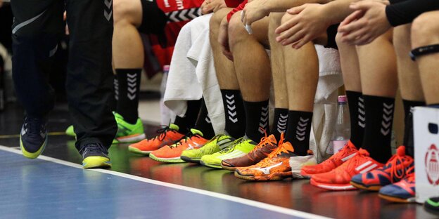 Männer sitzen auf der Bank am Hallenrand, sie tragen Handballschuhe und sind vom Knie abwärts zu sehen Männer sitzen auf der Bank am Hallenrand, sie tragen Handballschuhe und sind vom Knie abwärts zu sehen