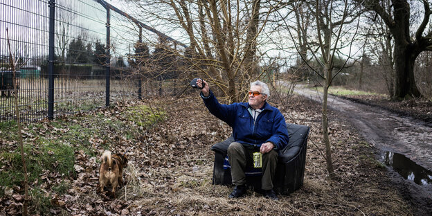 Ein Mann sitzt in einem Sessel und hat einen kleinen Hund an der Leine dabei