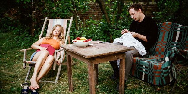 Eine Frau schläft im Garten in einem Liegestuhl, ein Mann näht etwas Eine Frau schläft im Garten in einem Liegestuhl, ein Mann näht etwas