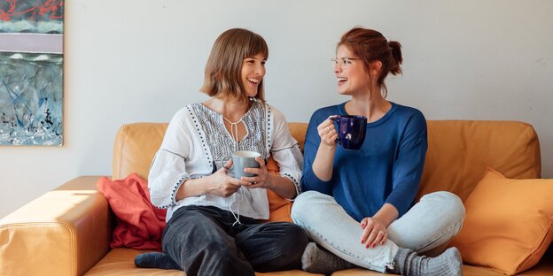 Zwei junge Frauen sitzen auf einem Sofa und trinken Tee Zwei junge Frauen sitzen auf einem Sofa und trinken Tee