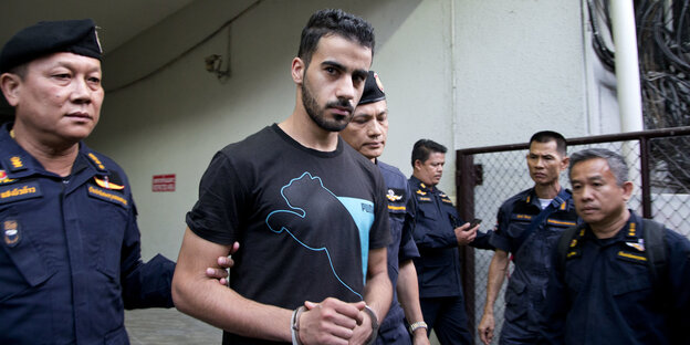 Ein junger Mann in T-Shirt und Handschellen wird von Polizisten begleitet Ein junger Mann in T-Shirt und Handschellen wird von Polizisten begleitet