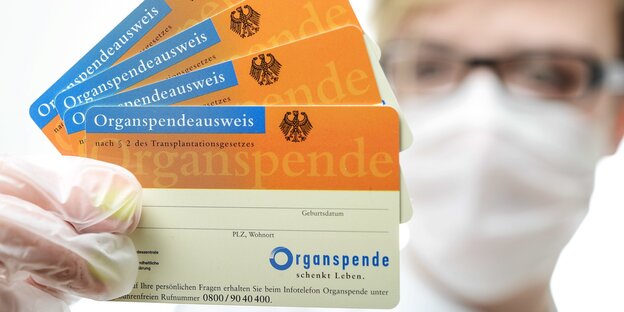 Eine Person mit Mundschutz und Handschuhen hält einen Organspendeausweis