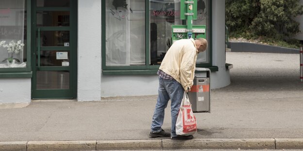 Ein Mann hat eine Plastiktüte in der Hand und hält seine Hand in einen Mülleimer Ein Mann hat eine Plastiktüte in der Hand und hält seine Hand in einen Mülleimer
