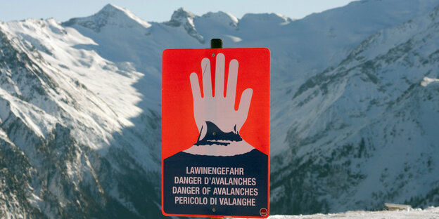 Ein Schild warnt vor einer Bergkulisse vor Lawinen. Ein Schild warnt vor einer Bergkulisse vor Lawinen.