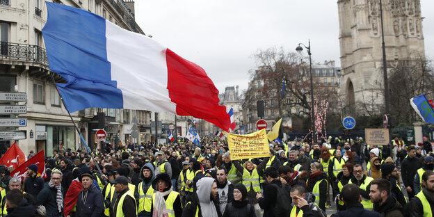 Teilnehmer einer «Gelbwesten»-Demonstration marschieren durch Paris, einer hält eine Frankreich-Flagge in die Höhe Teilnehmer einer «Gelbwesten»-Demonstration marschieren durch Paris, einer hält eine Frankreich-Flagge in die Höhe