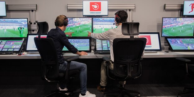 Zwei Männer sitzen vor Bildschirmen und schauen sich ein Fußballspiel an Zwei Männer sitzen vor Bildschirmen und schauen sich ein Fußballspiel an