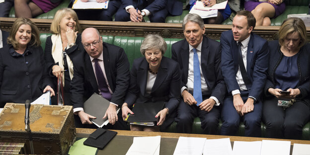 Theresa May sitzt zwischen mehreren Menschen auf einer Bank im House of Commons Theresa May sitzt zwischen mehreren Menschen auf einer Bank im House of Commons