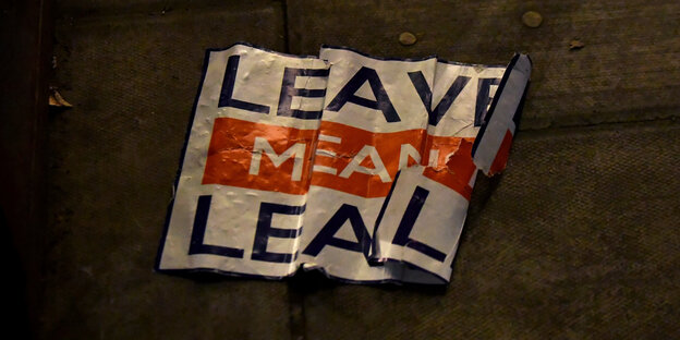 Auf einem zerknitterten Schild steht „Leave means leave“. Das Schild liegt auf dem Boden Auf einem zerknitterten Schild steht „Leave means leave“. Das Schild liegt auf dem Boden