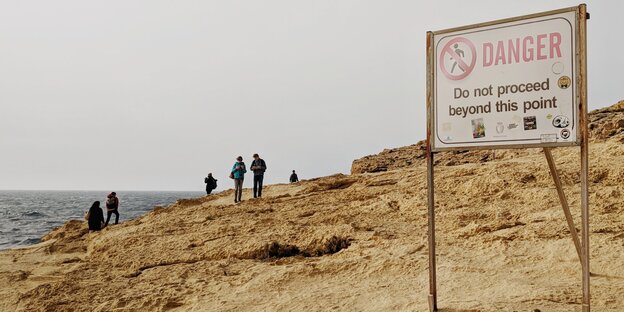 an einem Strand, mehrere Leute im Hintergrund, ein Schild mit Gefahrenwarnung im Vordergrund an einem Strand, mehrere Leute im Hintergrund, ein Schild mit Gefahrenwarnung im Vordergrund