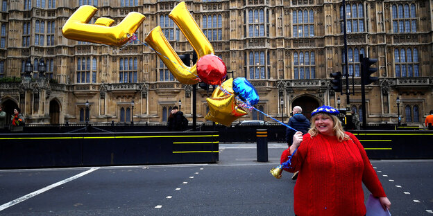 Frau im roten Pulli hält goldene Luftballons in Form der Buchstaben E und U in die Höhe Frau im roten Pulli hält goldene Luftballons in Form der Buchstaben E und U in die Höhe
