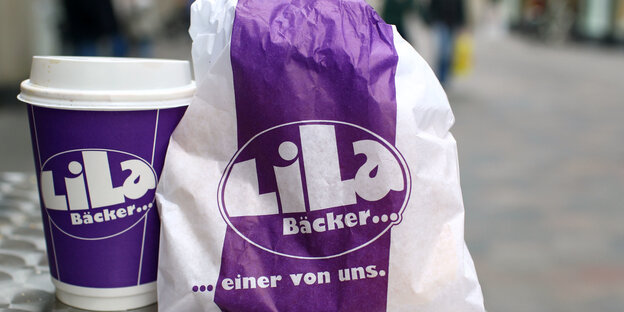Eine Tüte und Kaffee-Becher mit dem Logo der Lila Bäckerei. Eine Tüte und Kaffee-Becher mit dem Logo der Lila Bäckerei.